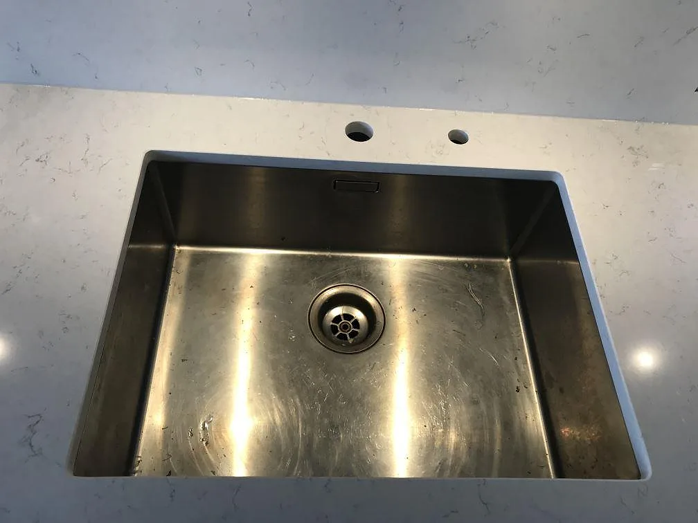 Underlimmad rostfri diskho i bänkskiva av Silestone Blanco Orion med två förborrade hål för blandare i ett kök i Jönköping.
