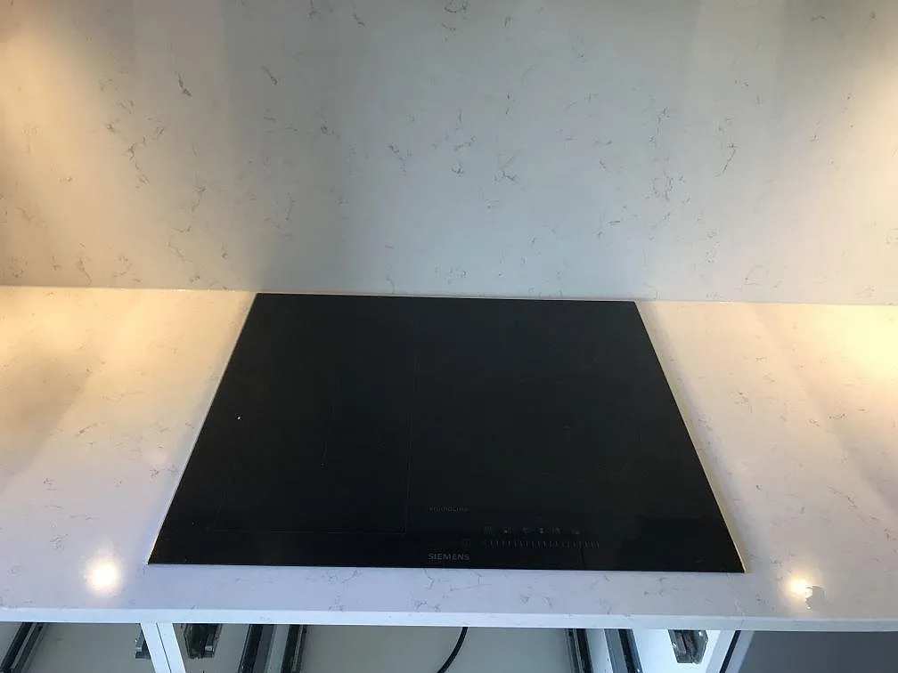 Infälld Siemens induktionshäll i bänkskiva av polerad Silestone Blanco Orion med stänkvägg bakom, kök i Jönköping.