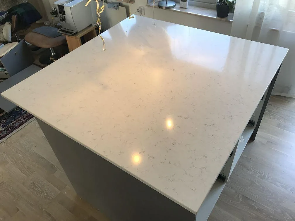 Köksö i vit Silestone Blanco Orion, polerad yta som speglar takspotsarna, i ett ljust kök i Jönköping.