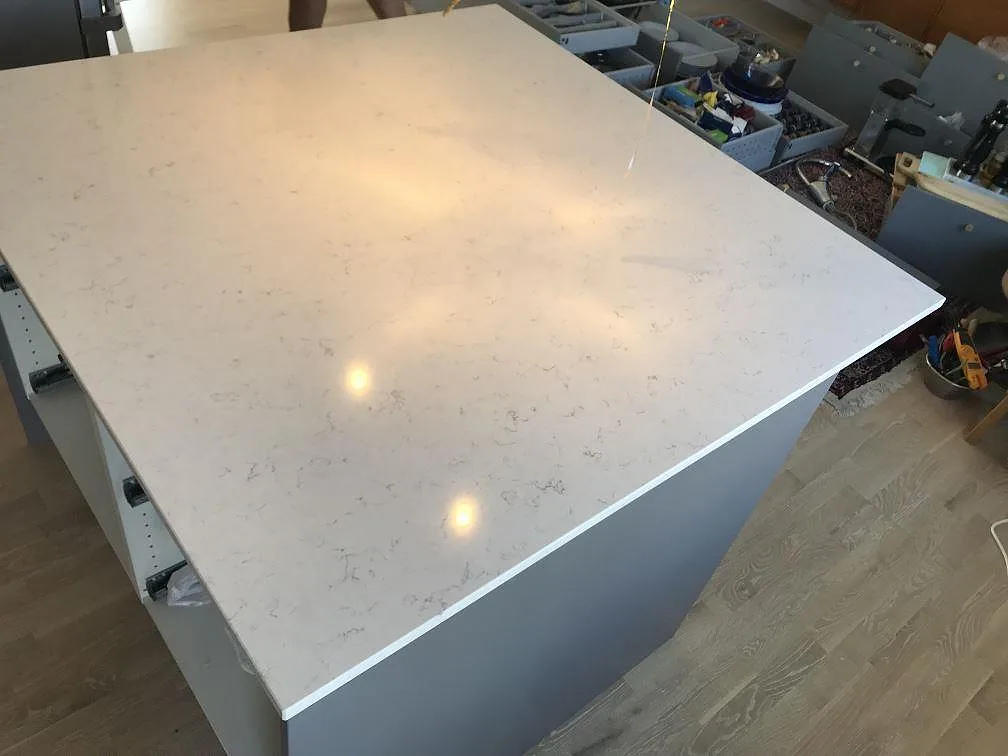 Kvadratisk köksö i polerad Silestone Blanco Orion på grå stomme i ett kök i Jönköping, vitt kvarts med diskret grå flammning.