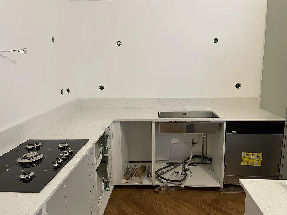 Köksbänkskiva i vit Silestone Blanco Orion, polerad, i ett L-format kök under montering med övermonterad gashäll och underlimmad diskho i Malmö.