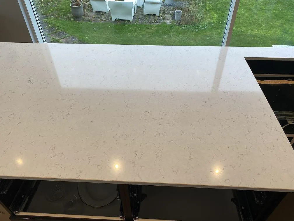 Detalj av polerad Silestone Blanco Orion köksö med ljus grå ådring och reflektion från fönster i Malmö.