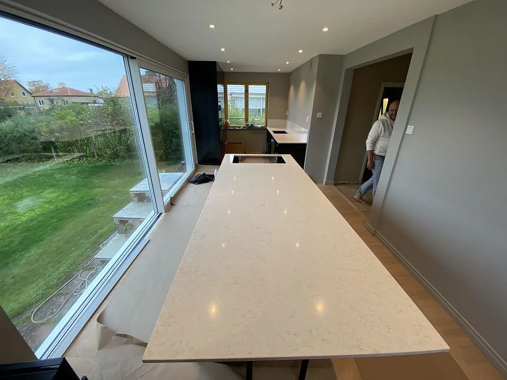 Lång köksö med polerad köksbänkskiva i Silestone Blanco Orion komposit i ett kök i Malmö under montering.