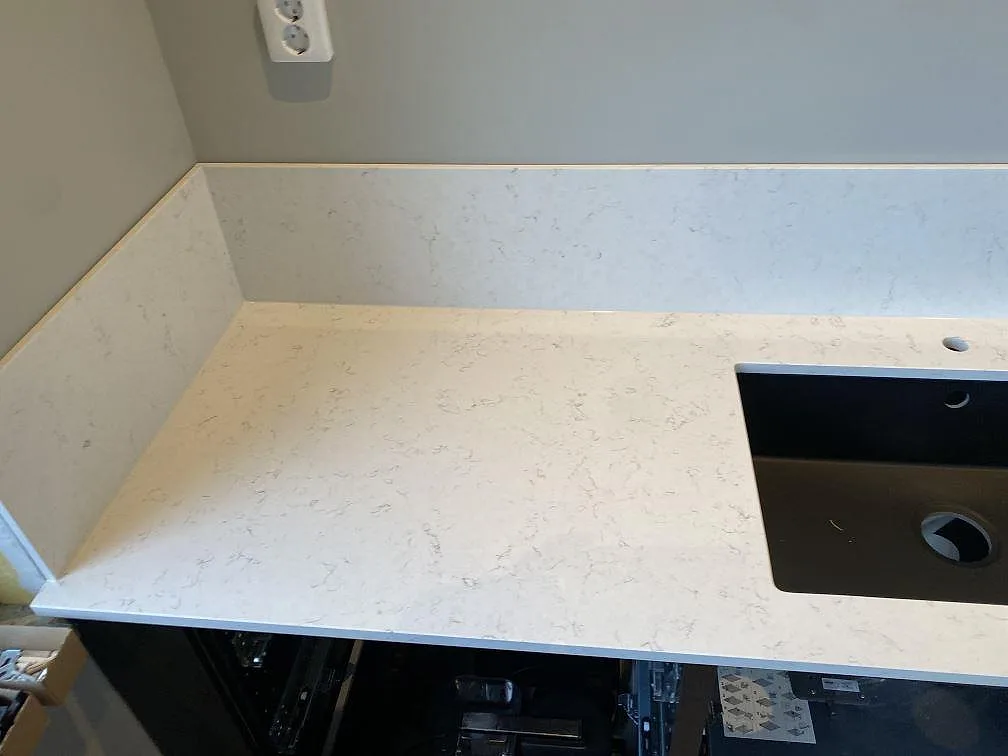 Köksbänkskiva i polerad Silestone Blanco Orion med låg uppvikt stänkkant och mörk rektangulär öppning i Malmö.