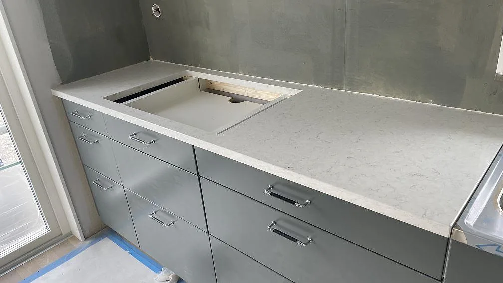Köksbänkskiva i ljus Silestone Blanco Orion, polerad kvartskomposit med fint grått stänk, med underlimmad ho och separat borrat blandarhål under montering i ett kök i Nol.
