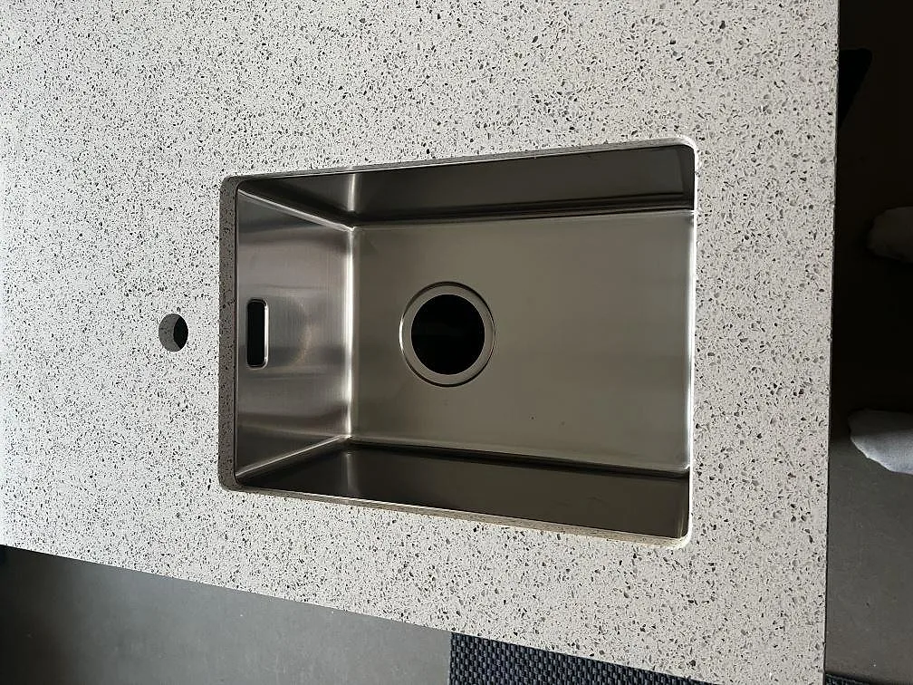 Närbild på underlimmad rostfri diskho i polerad Silestone Blanco Stellar, vit kompositbänkskiva i Tvååker.