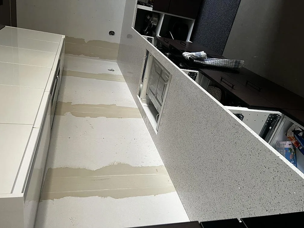 Lång bänkskiva i polerad Silestone Blanco Stellar längs mörka köksstommar under montering i Tvååker.
