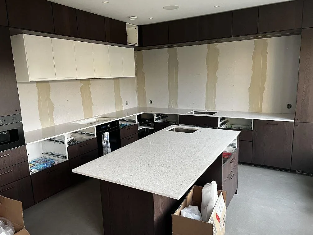 Köksbänkskiva och köksö i polerad Silestone Blanco Stellar, vit kvartskomposit, under montering i ett kök i Tvååker.
