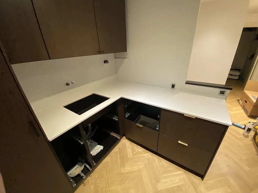 Köksbänkskiva i vit Silestone Blanco Zeus Extreme, polerad, i L-format med underlimmad svart kompositdiskho i ett kök i Rödovre.