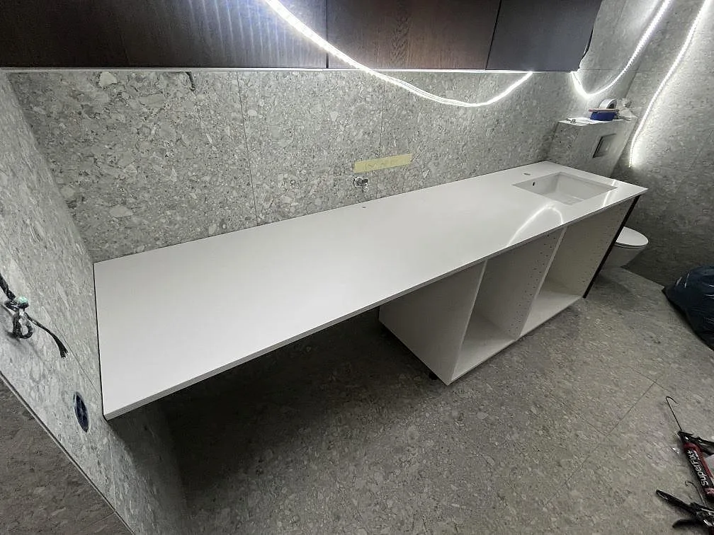 Badrumsbänkskiva i vit Silestone Blanco Zeus, polerad kvartskomposit, monterad som lång skiva över öppna stommar i Huddinge.