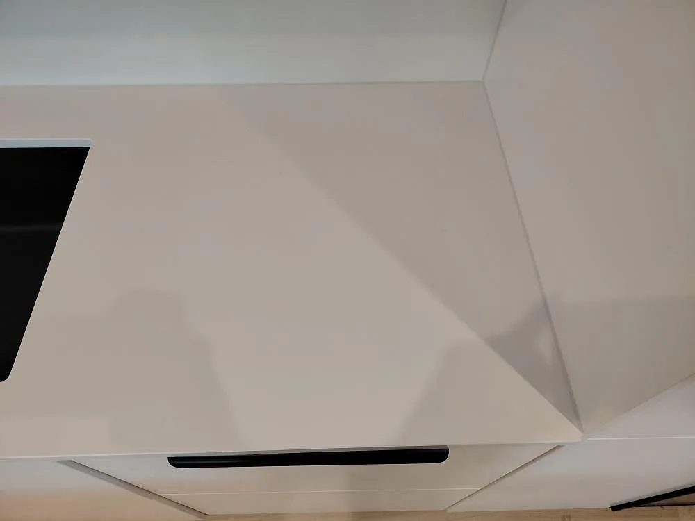 Närbild på polerad Silestone Blanco Zeus bänkskiva med vitt stänkskydd och svart hällkant i ett kök i Västerås.