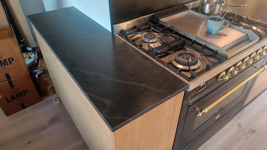 Matt Silestone Bohemian Flame som köksbänkskiva bredvid en fristående gasspis och träinredning i ett kök i Kävlinge.