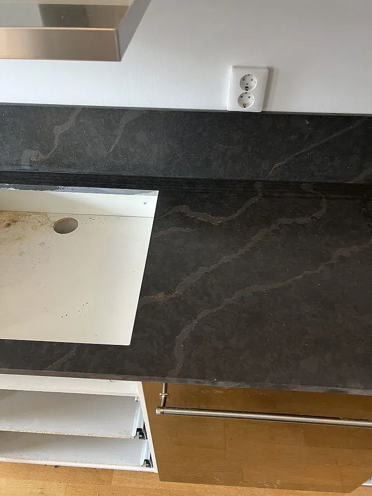 Detalj av mörk Silestone Bohemian Flame med hällöppning, stänkskydd och vita köksstommar i Limhamn.