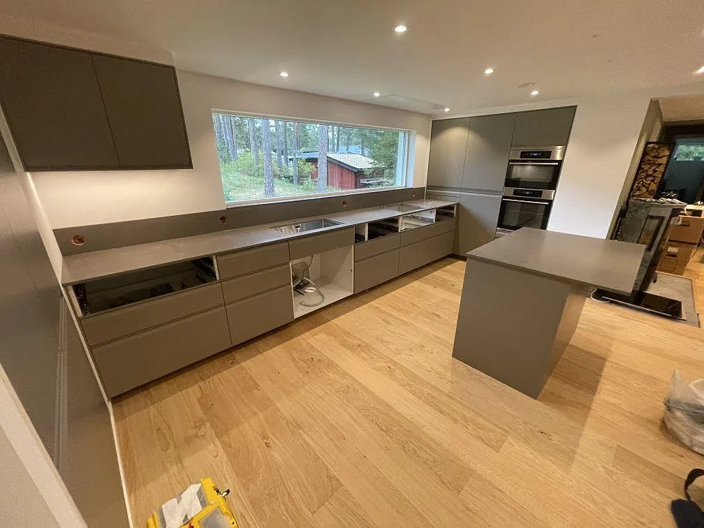 Kök i Åhus med lång bänkskiva och köksö i Silestone Brass Relish, matt Mocka komposit, under montering.