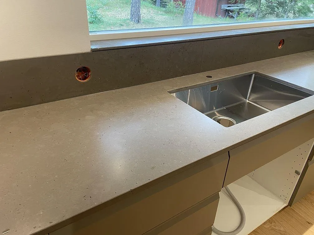 Närbild på underlimmad rostfri diskho i bänkskiva av Silestone Brass Relish, matt Mocka komposit, med stänkskydd i Åhus.