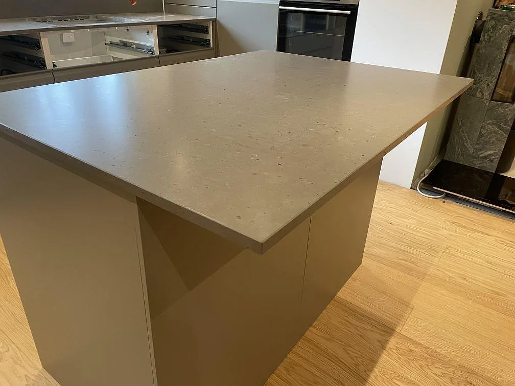 Närbild på köksö eller halvö i Silestone Brass Relish, matt Mocka komposit, med beige köksstommar i Åhus.