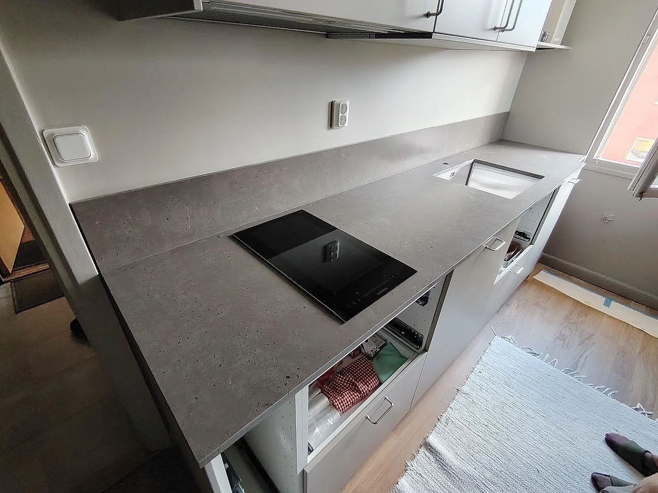Köksbänkskiva i grå taupe Silestone Brass relish, matt Mocka-yta, med induktionshäll och uppvikt stänkskydd i ett kök i Årsta.