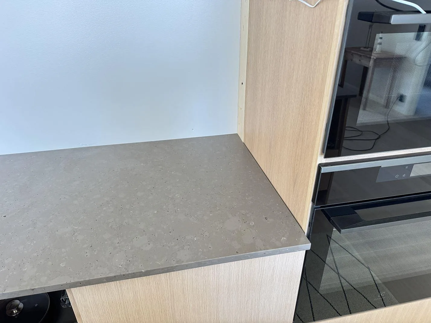 Detalj av matt Silestone Brass relish bänkskiva vid ugnsskåp med gråbrun komposityta i Glommen.