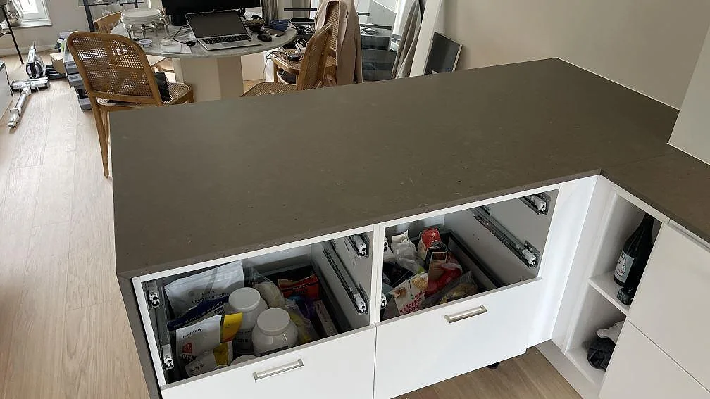 Matt Silestone Brass relish som L-formad köksbänkskiva över vita stommar i ett kök under montering i Hjärup.