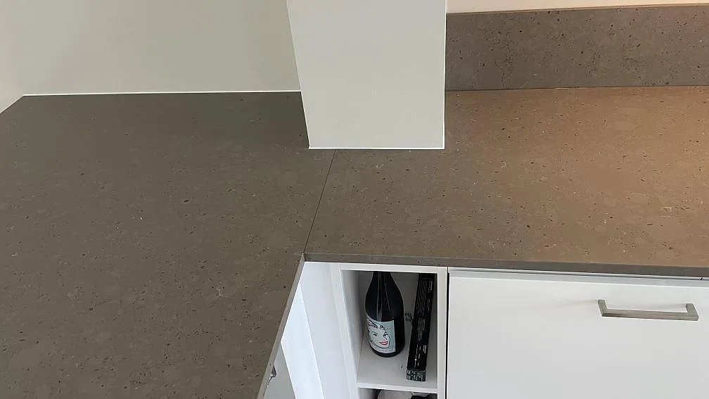 Lång väggbänk i matt Silestone Brass relish med lågt stänkskydd och vit köksinredning under montering i Hjärup.