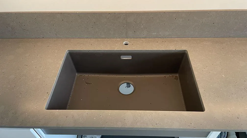 Detalj av mörk ho, kranhål och stänkskydd i matt Silestone Brass relish kvartskomposit i Hjärup.
