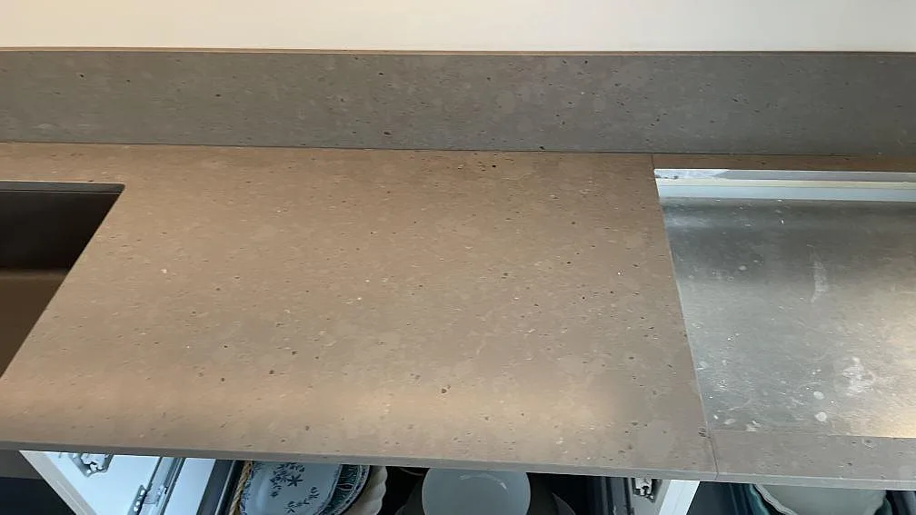 Detalj av matt Silestone Brass relish arbetsyta med stänkskydd och finprickig gråbrun struktur i Hjärup.