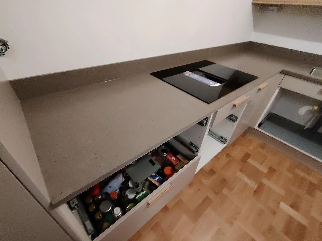 Matt Silestone Brass relish komposit vid induktionshällen i ett L-format kök med vita stommar och träparkett i Stockholm.