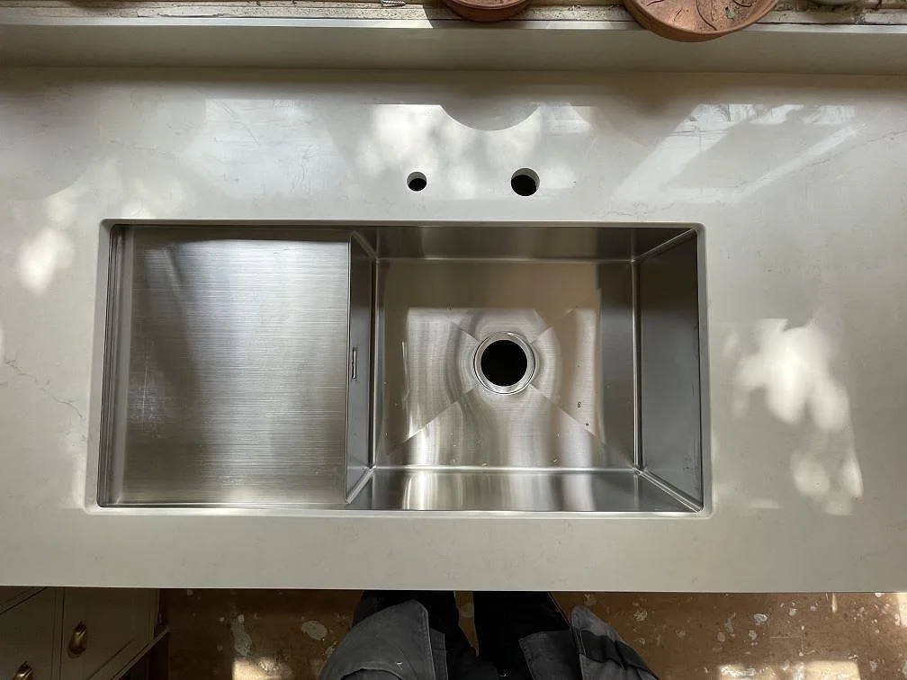 Underlimmad rostfri diskho med stor ho och mindre tråg infälld i polerad Silestone Calacatta Tova bänkskiva, med två förborrade blandarhål, i ett kök i Bagarmossen.