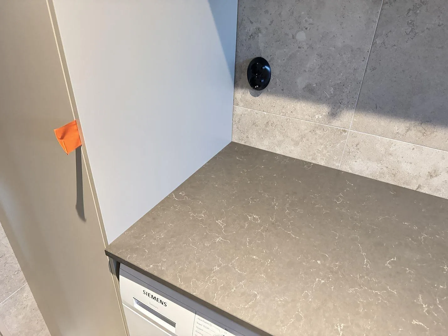 Detalj av grå Silestone Calypso i matt kvartskomposit ovanför tvättmaskin och kaklad vägg i ett våtrum i Alingsås.