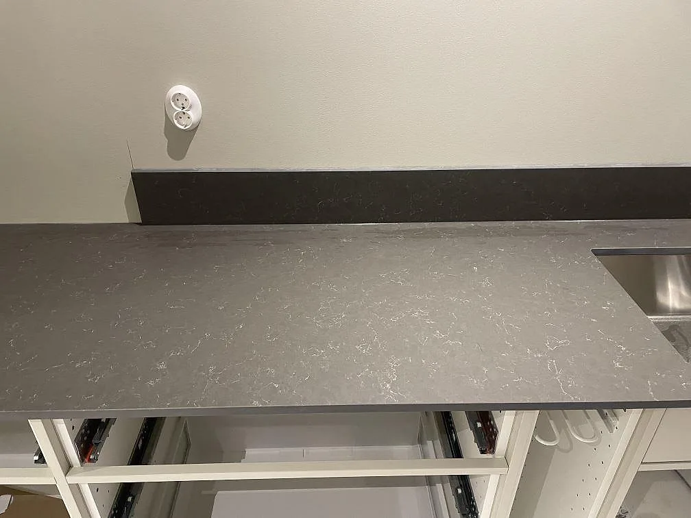 Köksbänkskiva i grå Silestone Calypso, matt Mocka-finish med diskret ljus ådring och uppvikt stänkkant, i ett kök under montering i Heberg.