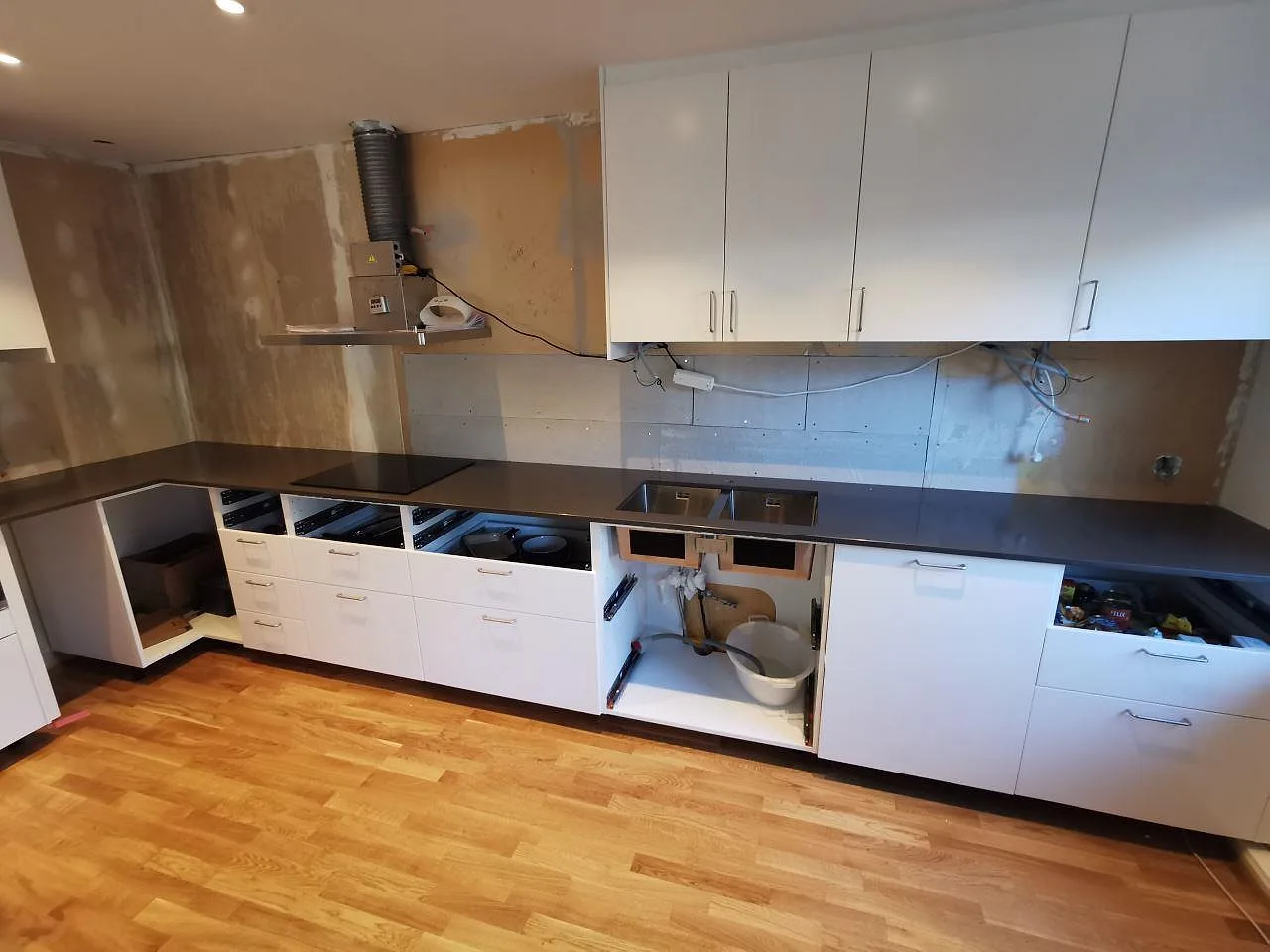 Köksbänkskiva i mörk polerad Silestone Calypso längs en lång rak köksrad i ett kök under montering i Hovås, med underlimmad rostfri diskho och induktionshäll.