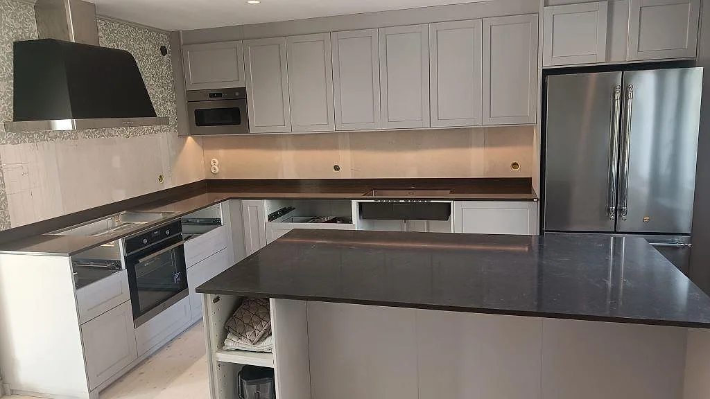 Köksbänkskiva och stor köksö i polerad Silestone Calypso, mörk kvartskomposit, monterad i ett kök i Lund med stänkkant längs väggen.