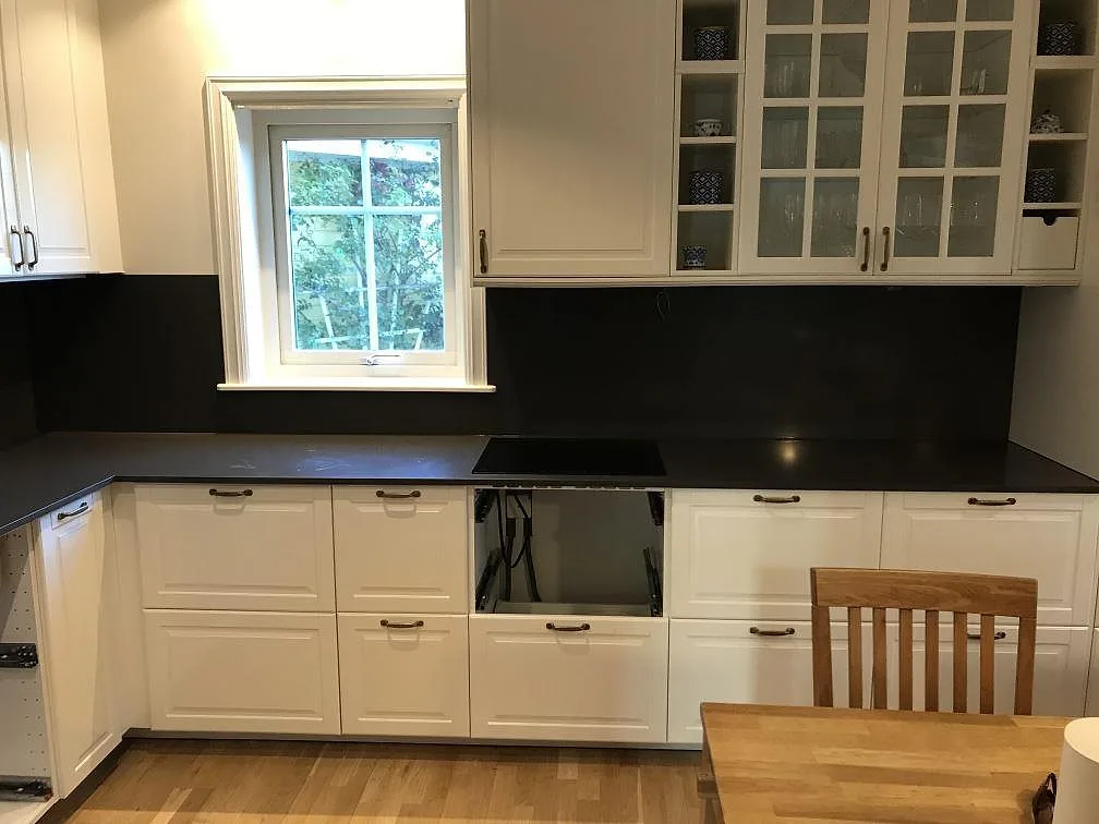 Köksbänkskiva i mörkgrå Silestone Calypso, polerad, med häll och stänkskydd i ett vitt kök i Mölndal.