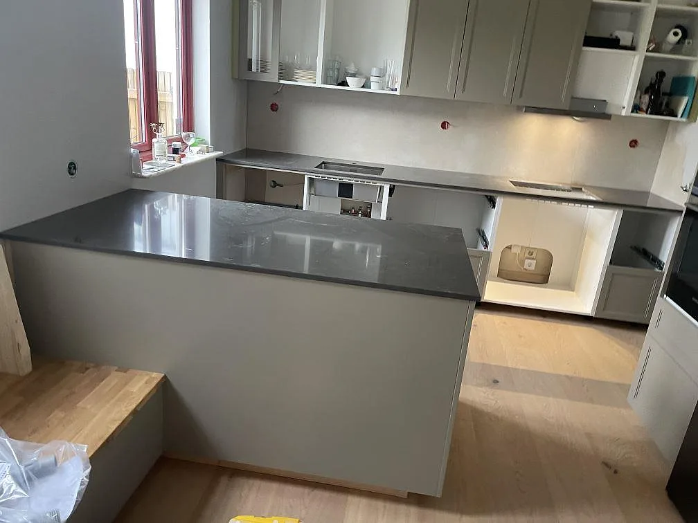 Bred köksvy med polerad Silestone Calypso på köksö och bakre bänkrad under montering i Vintrie.