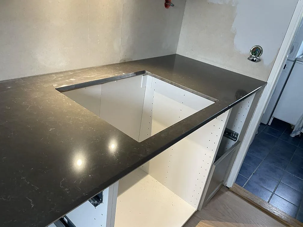 Hörndel av köksbänkskiva i Silestone Calypso med öppet hälluttag och vit köksstomme i Vintrie.