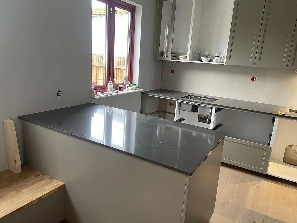 Köksbänkskiva i grå Silestone Calypso, polerad komposit, med stor köksö och rostfri diskho i ett kök i Vintrie.