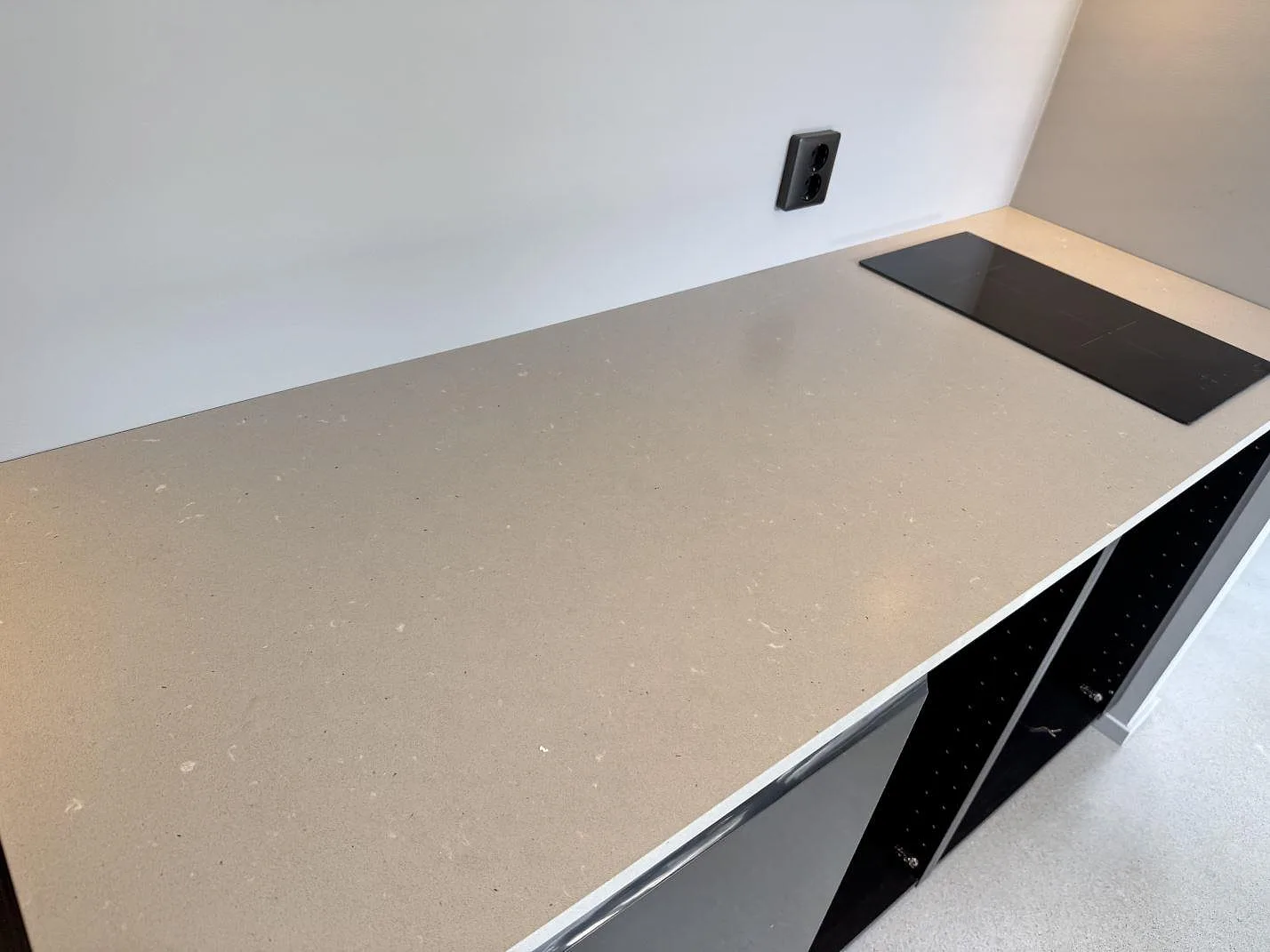 Köksbänkskiva i Silestone Camden, matt Mocka-kvartskomposit, med svart häll på en rak bänkrad i ett kök i Höllviken.