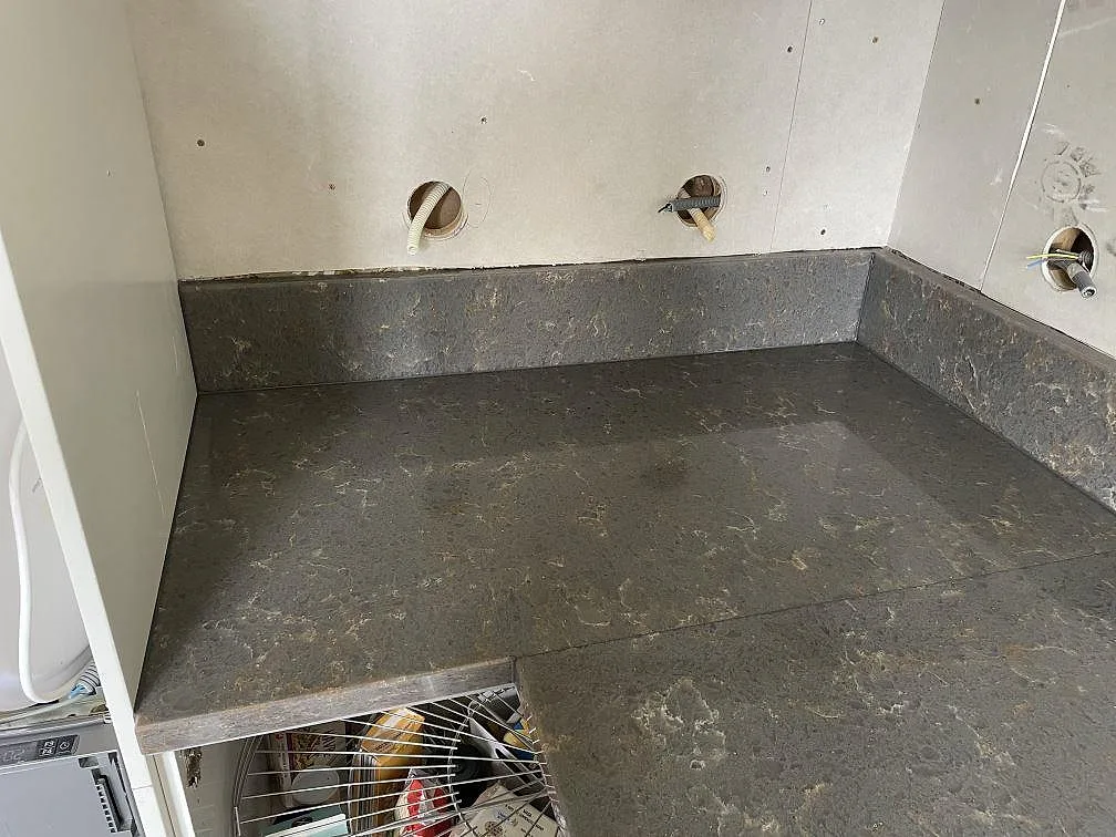 Köksbänkskiva i Silestone Cooper Mist, grå-taupe kvartskomposit med uppvikt stänkkant, i ett kök under montering i Lerum.