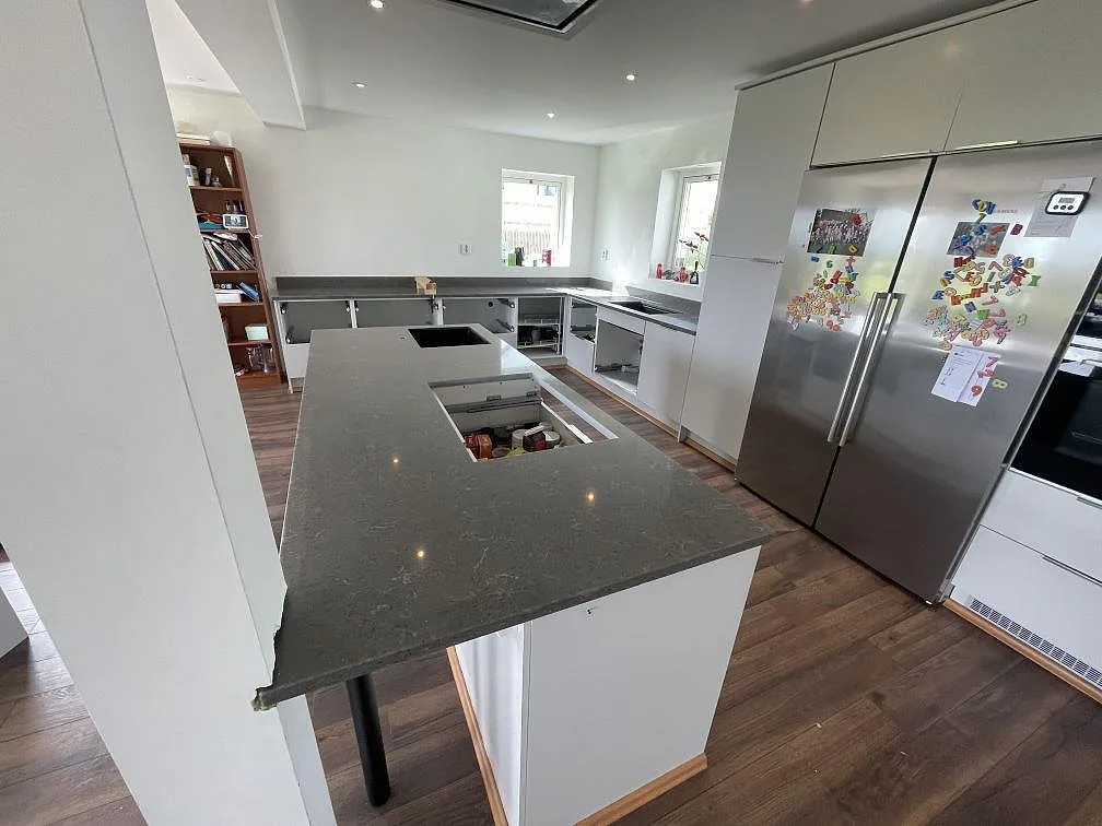Köksbänkskiva i Silestone Cooper Mist, polerad grå komposit, i ett U-format kök med halvö och förberedd hällöppning i Ystad.
