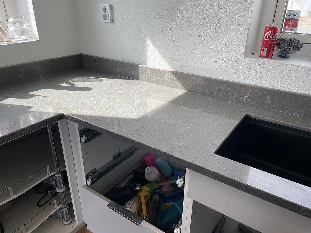 Hörndel av köksbänkskiva i Silestone Cooper Mist med stänkkant och svart diskho, polerad komposit i Ystad.