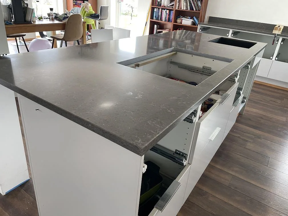 Polerad köksbänkskiva i Silestone Cooper Mist med svart underlimmad diskho och hällöppning i ett kök under montering i Ystad.