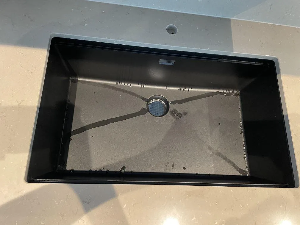 Närbild på svart underlimmad diskho i polerad Silestone Coral Clay bänkskiva med beige yta i Skurup.