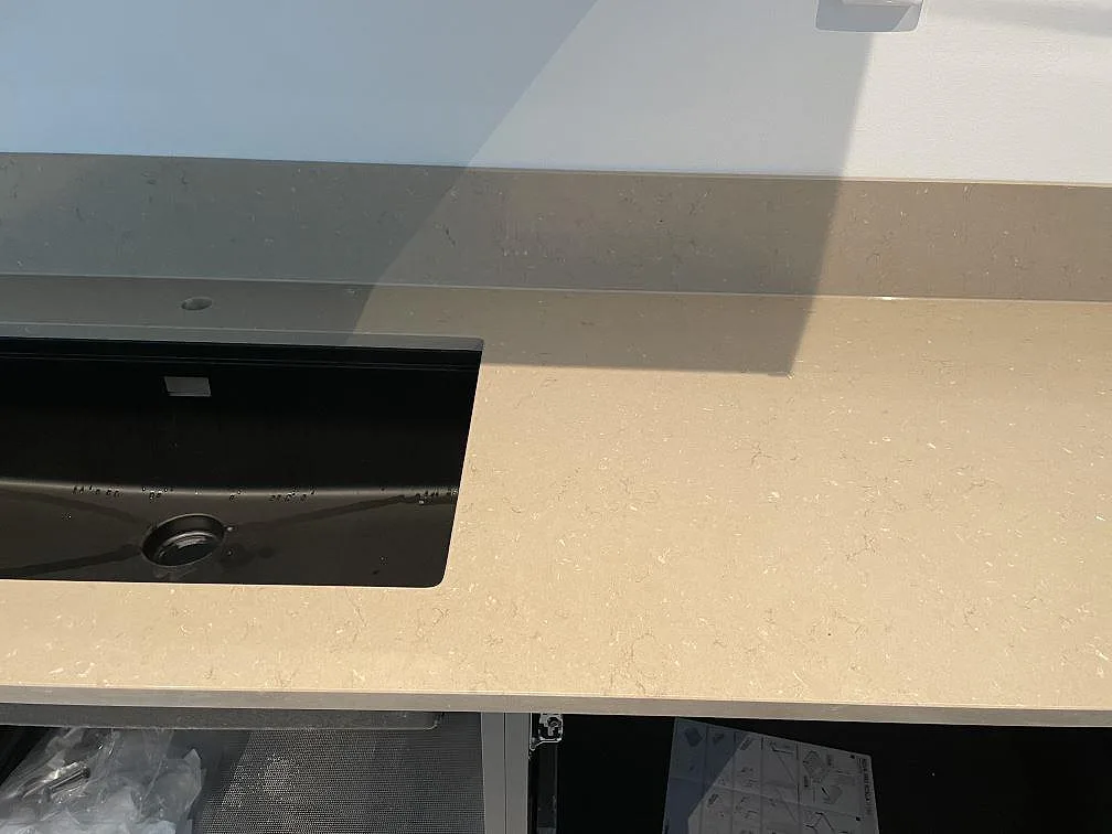 Detalj av polerad Silestone Coral Clay bänkskiva med svart diskho och uppvikt stänkkant under montering i Skurup.