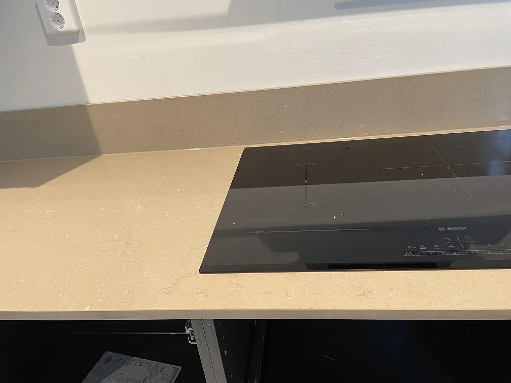 Polerad Silestone Coral Clay bänkskiva med Bosch induktionshäll och gråbeige stänkkant i ett kök i Skurup.