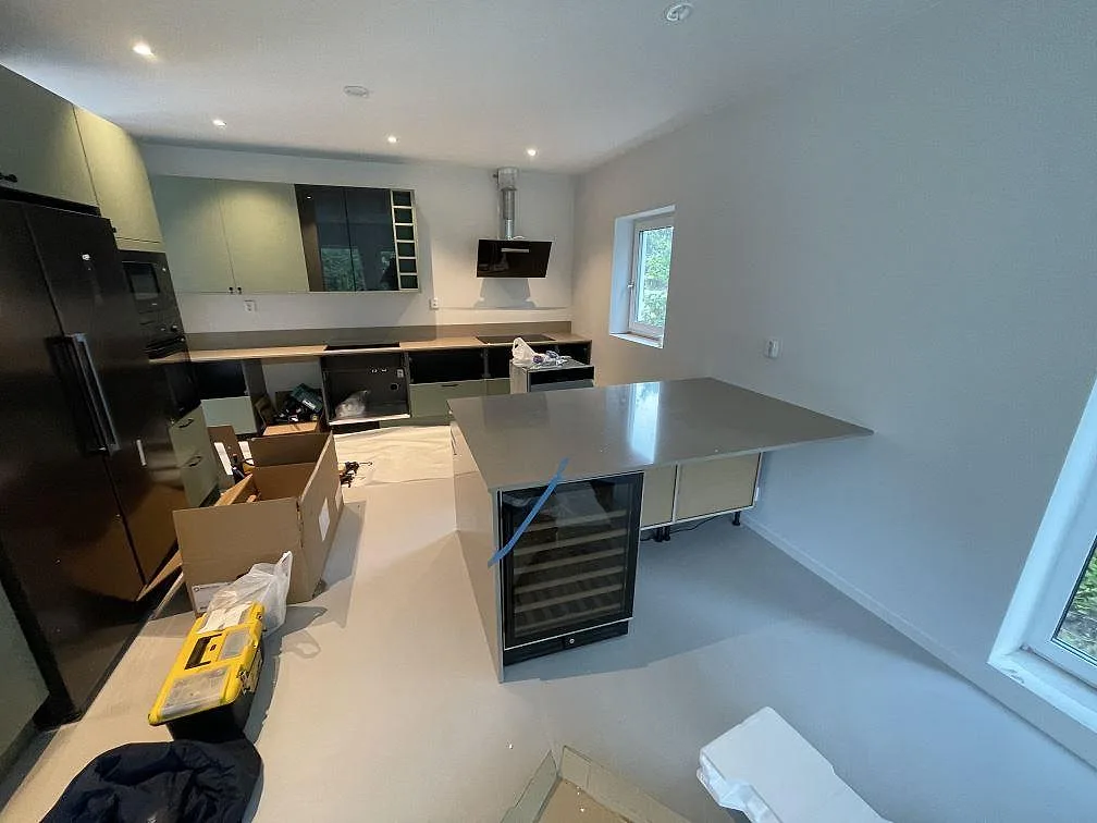 Öppet kök i Skurup med polerade Silestone Coral Clay bänkskivor, stor köksö, vinkyl och pågående montering.