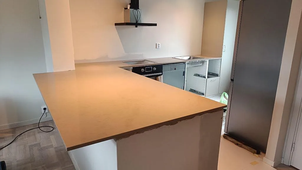 Köksbänkskiva i polerad Silestone Coral Clay komposit med bred halvö och diskhoområde i ett kök i Åhus.