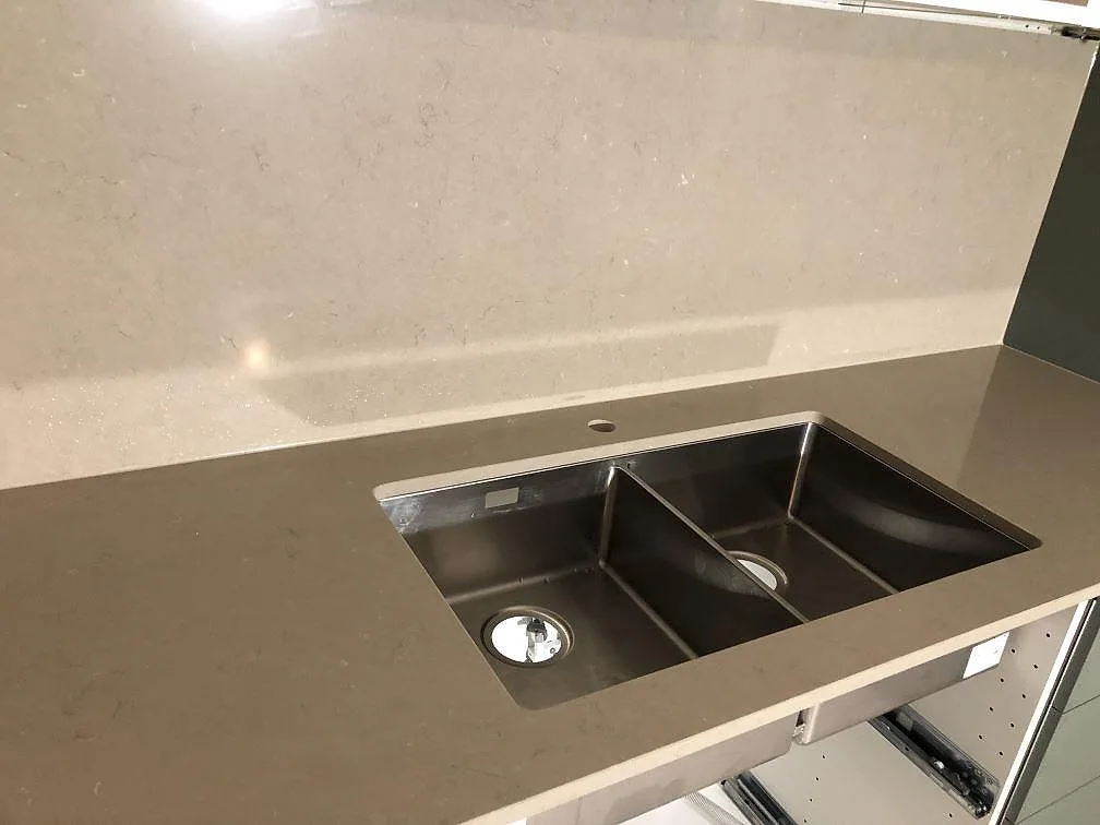 Underlimmad dubbel rostfri diskho i en polerad köksbänkskiva i Silestone Coral Clay med uppvikt stänkkant i samma sten i ett kök i Åkarp.