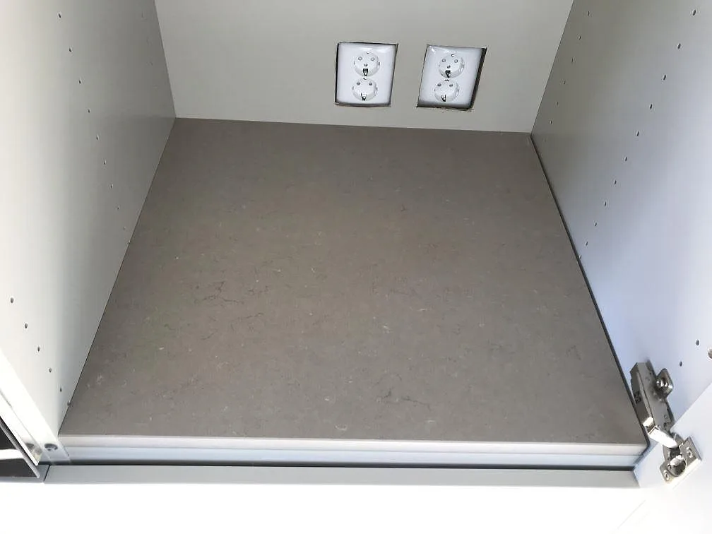 Bänkskiva i matt Silestone Coral Clay längs fönstret med eluttag i väggen i ett kök i Åsa.