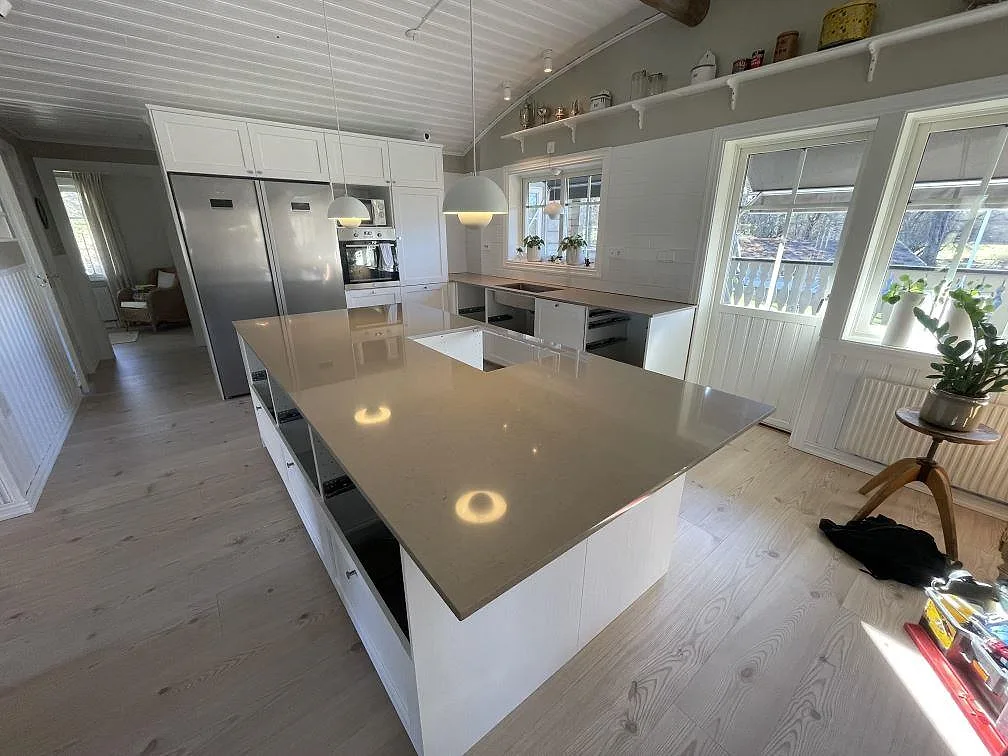 Stor köksö i Silestone Coral Clay, polerad, i ett ljust kök med vita luckor och välvt pärlsponttak i Älmhult.
