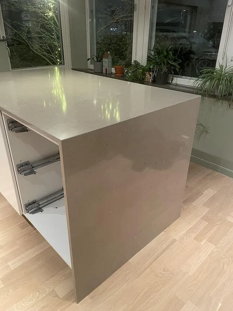 Köksö i Silestone Coral Clay, polerad beige kvartskomposit, monterad i ett kök med trägolv i Älta under pågående montering.